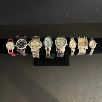 Collection of women's wristwatches displayed on a black velvet t-bar stand, featuring various bezel shapes, leather straps, and...