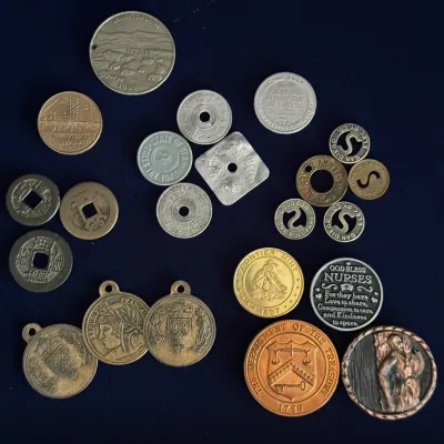 Collection of vintage tokens, medals, and coins, including state sales tax tokens, transit tokens, and commemorative pieces.