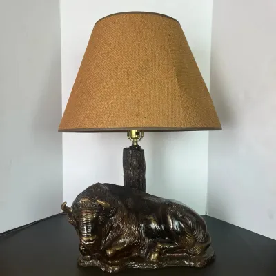 Sale Photo Thumbnail #104: Vintage table lamp featuring a sculpted reclining bison or buffalo base with a textured tree trunk column and a woven burlap shade.