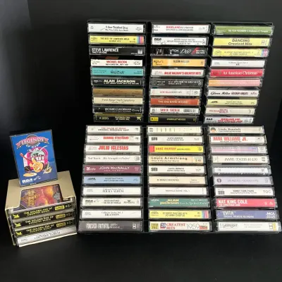 Large collection of cassette tapes featuring classic country, big band, jazz, and pop music, displayed in black plastic storage racks.