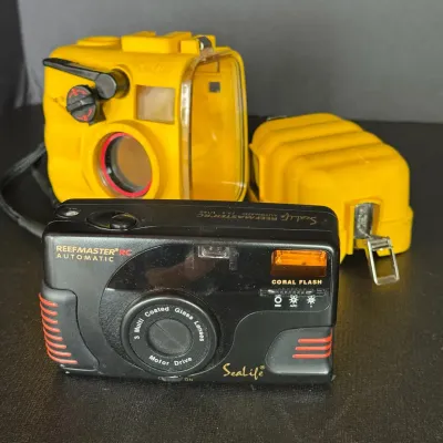 Sale Photo Thumbnail #108: SeaLife Reefmaster RC Automatic 35mm underwater camera set, including the black camera body and yellow waterproof housing.