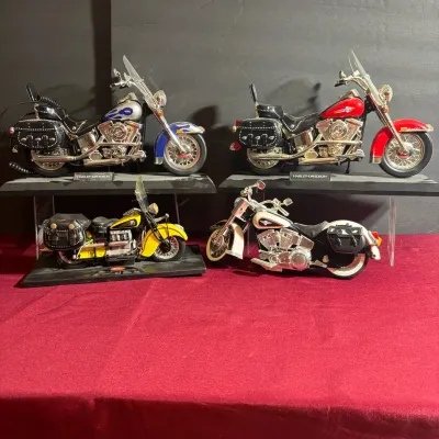 Collection of four die-cast scale model motorcycles, including Harley-Davidson and Indian models, displayed on acrylic risers against a...