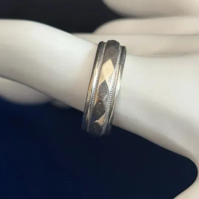 Vintage white metal wedding band featuring milgrain borders and engraved detailing, displayed on a mannequin hand model.