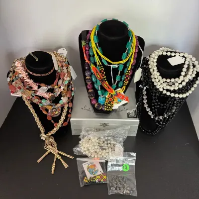Collection of costume jewelry displayed on three black velvet busts, including beaded, faux pearl, and stone statement necklaces...