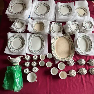 Large vintage porcelain dinnerware service set featuring a floral and bird motif, laid out on a red surface with protective foam and...