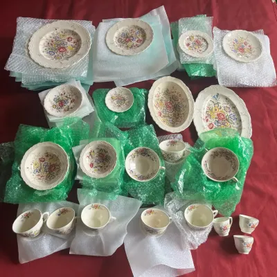 Vintage floral pattern china dinnerware set, including plates, bowls, teacups, and serving pieces, wrapped for transport.