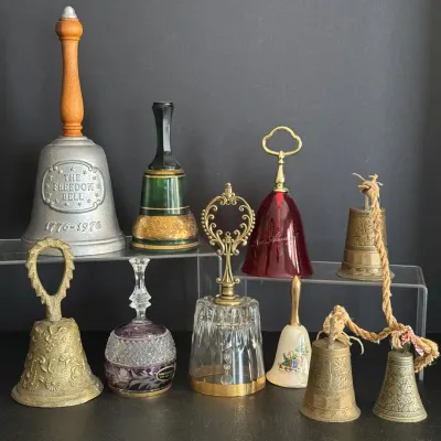 Collection of vintage decorative hand bells in brass, glass, crystal, and metal, featuring a 1976 Bicentennial Freedom Bell.