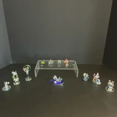 Collection of miniature crystal and glass figurines displayed on a dark surface and clear acrylic riser.