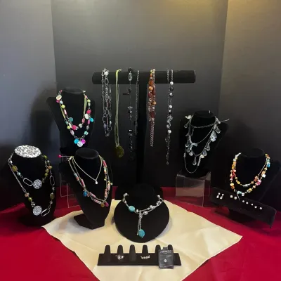 An assortment of colorful costume jewelry, including beaded, statement, and Y-drop necklaces, displayed on black velvet stands and T-bars...