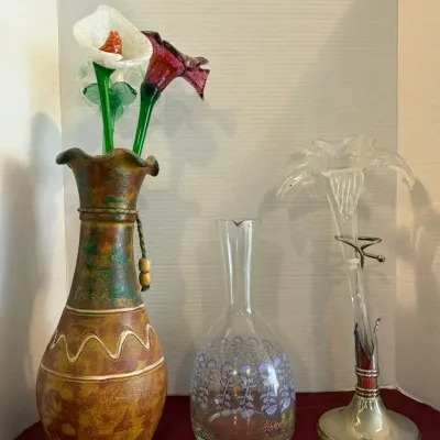 Collection of decorative vases and art glass including a tall textured ceramic vase holding glass calla lilies, a clear glass decanter...