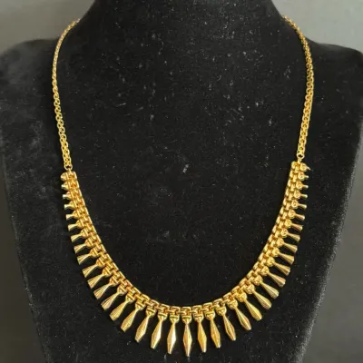 Gold-tone vintage fringe necklace featuring teardrop-shaped dangling accents attached to an articulated chain, presented on a black...