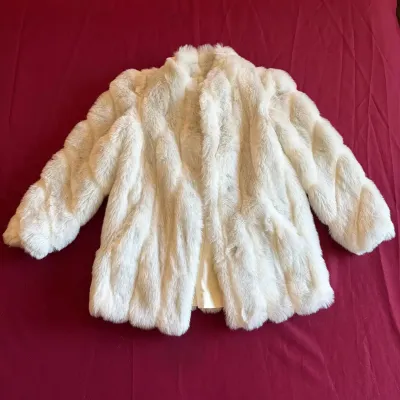 Vintage white faux fur waist-length jacket with a shawl collar, laid flat on a red surface.