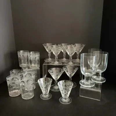 Collection of mid-century etched crystal glassware, including cocktail coupes, tumblers, and footed glasses with floral patterns.