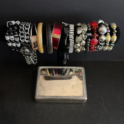 Assortment of modern and vintage costume bracelets displayed on a T-bar stand alongside a mirrored silver-tone trinket box.