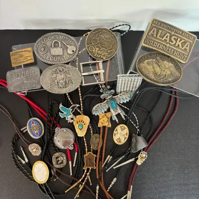 Collection of vintage belt buckles and bolo ties featuring Southwestern, Native American-style, motorcycle, and outdoorsman themes.