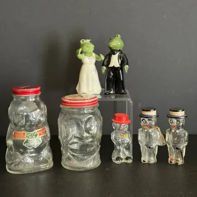 Collection of vintage glass jars and novelty figurines, featuring a Dutch Little Pig mustard jar, a molded face jar, novelty glass salt...