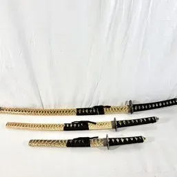 Sale Photo Thumbnail #5: Three-piece Japanese samurai sword set, including katana, wakizashi, and tanto with matching ornate gold-tone scabbards and black tsuka-ito wrapped handles.