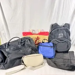 Sale Photo Thumbnail #174: Assorted collection of bags including a black duffel bag, a Mazda branded backpack, a blue lunch tote, a straw tote with red trim, and a cream belt bag.