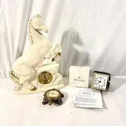Sale Photo Thumbnail #140: Vintage off-white ceramic rearing horse clock featuring gold accents, displayed alongside a small brass turtle clock and a Bulova travel alarm clock with its original box and manual.