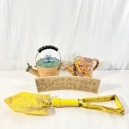 Sale Photo Thumbnail #167: Collection of garden decor and tools, including two ceramic watering pots, a painted stone plaque, and a yellow folding entrenching shovel.