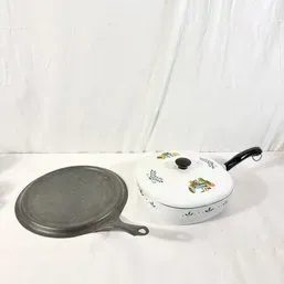 Sale Photo Thumbnail #56: Vintage cookware including a round cast iron griddle pan alongside a lidded white enamel skillet with printed floral and figure motifs.