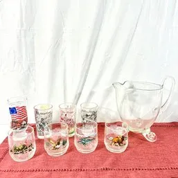 Sale Photo Thumbnail #149: Vintage clear glass beverage set featuring a footed pitcher and a variety of printed tumbler and lowball glasses with wildlife and Patriotic motifs.