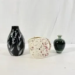 Sale Photo Thumbnail #20: Collection of three art pottery pieces, including a black bottle vase with white botanical etchings, a cream speckled pitcher, and a small dark green glazed bud vase.