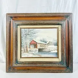 Sale Photo Thumbnail #247: Framed winter landscape painting depicting a red covered bridge over a river, set in a heavily molded rustic wood frame with an inner cream mat.
