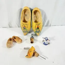 Sale Photo Thumbnail #115: Collection of Dutch wooden clogs and souvenirs, including hand-painted yellow wooden shoes labeled 'Volendam' and 'Holland', miniature clogs, bottle stoppers, and a blue and white Delftware figurine.