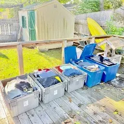 Sale Photo Thumbnail #81: Selection of plastic storage totes and crates filled with various clothing items, displayed outdoors on a wooden deck.