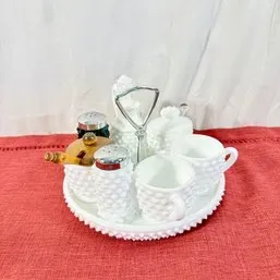 Sale Photo Thumbnail #177: Vintage white milk glass hobnail breakfast or tea caddy set, featuring small cups, salt and pepper shakers, and lidded jars arranged on a matching tray with a central metal handle.