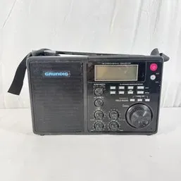 Sale Photo Thumbnail #91: Vintage Grundig portable shortwave field radio featuring a black case, digital LCD screen, carry strap, and multiple tuning controls.