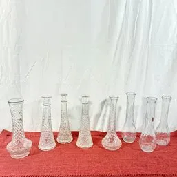 Sale Photo Thumbnail #32: Collection of eight vintage clear glass bud vases in various pressed and smooth styles, displayed on a red surface.