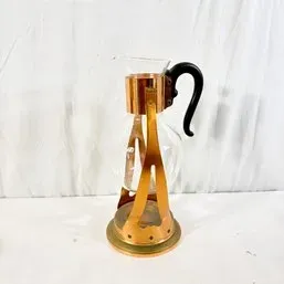 Sale Photo Thumbnail #88: Vintage glass coffee carafe with a copper and brass stand and a curved black plastic handle, mid-20th century.