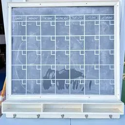 Sale Photo Thumbnail #27: Framed wall-mounted chalk calendar featuring a monthly grid, lower storage cubbies, and five metal hanging hooks underneath.
