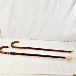 Sale Photo Thumbnail #156: Pair of vintage bentwood wooden walking canes, one featuring a leather wrap detail and rubber tip, and the other with a tapered metal tip.