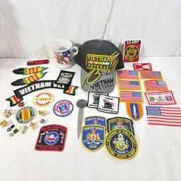 Sale Photo Thumbnail #238: Collection of military and law enforcement memorabilia, including Vietnam Veteran embroidered patches, American flag patches, lapel pins, a baseball cap, and a mug.