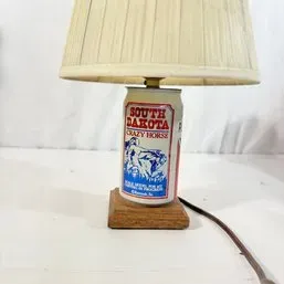 Sale Photo Thumbnail #21: Novelty table lamp crafted from a South Dakota Crazy Horse commemorative aluminum can set on a wooden base with a pleated fabric shade.