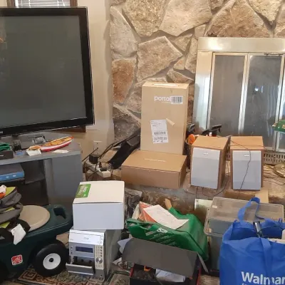 Living room assortment featuring a large Samsung flat-screen TV on a media stand, a Step2 rolling garden scooter, electronics, and...