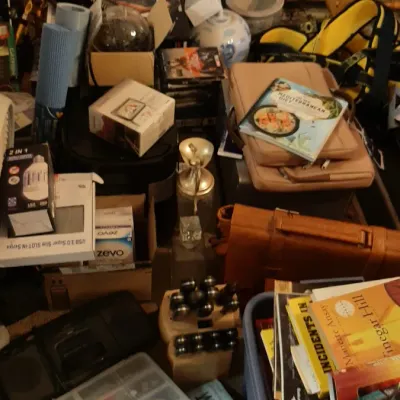 Cluttered assortment of household goods, including books, blue-and-white porcelain ginger jars, boxed electronics, a knife block, and...