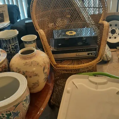Vintage woven wicker peacock armchair holding a vintage record player stereo system, displayed alongside assorted decorative Asian-style...