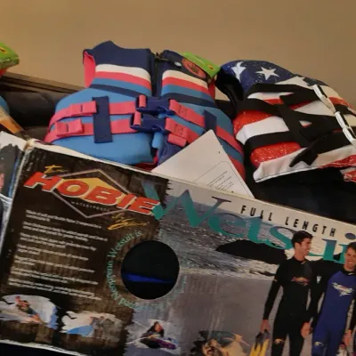 Selection of modern life jackets alongside a vintage Hobie full-length wetsuit in its original box.