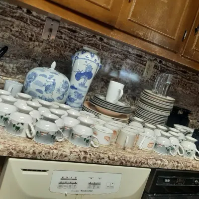A large assortment of vintage tableware displayed on a kitchen counter, including blue and white porcelain vases, multiple tea cups, and...