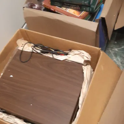 Cardboard storage boxes containing vintage electronics with woodgrain cabinet and assorted hardcover reference books.