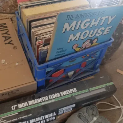 Blue plastic crate packed with vintage vinyl records, featured alongside a copy of 'The Adventures of Mighty Mouse' album.