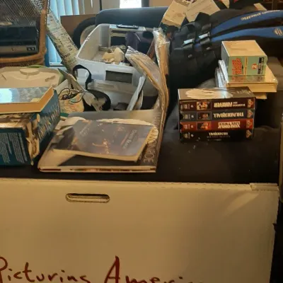 Collection of assorted household media and collectibles, including VHS tapes, books, a vintage Royal typewriter, and storage containers.
