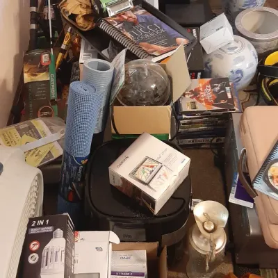 Assorted household clutter including a boxed Garmin GPS unit, a Tucci Cookbook, fishing rods, yoga mats, and Asian-style ginger jars.