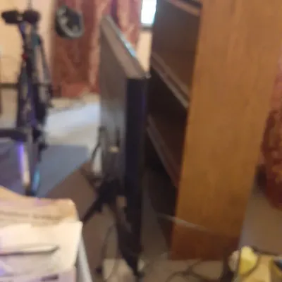 Black flat-screen television placed on the floor next to a tall wooden bookcase and an exercise bike.