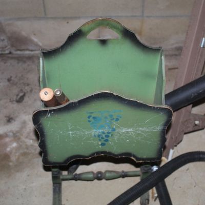 Sale Photo Thumbnail #106: Vintage green painted wooden magazine rack featuring a blue stenciled grape motif and turned spindle base, showing surface wear and scuffs.