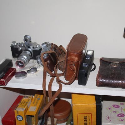 Sale Photo Thumbnail #87: Collection of vintage cameras and leather cases displayed on a shelf, alongside various boxed photography equipment.